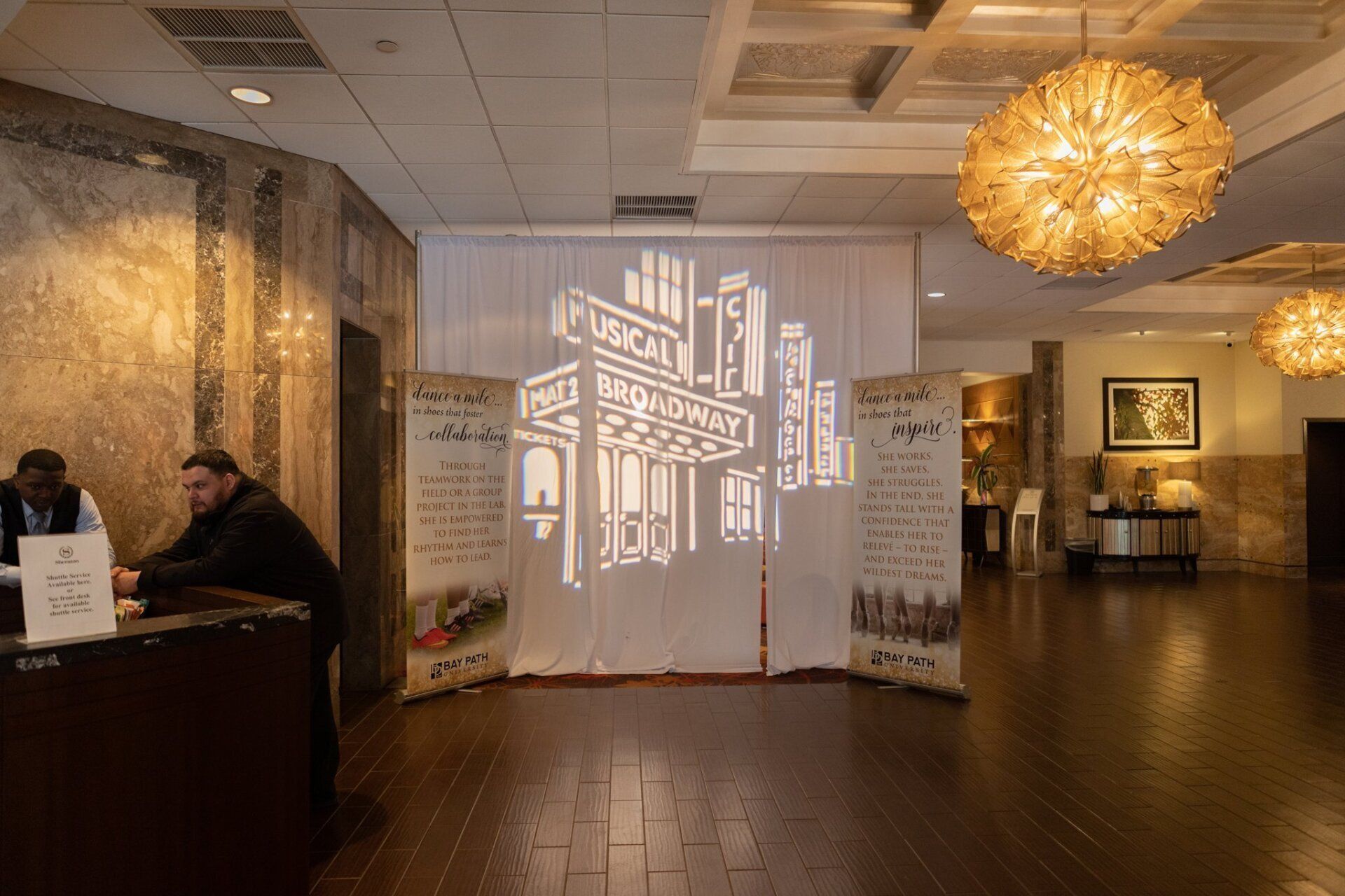 Indoor lobby with a white sculptural display, warm lighting, and people at a reception desk.