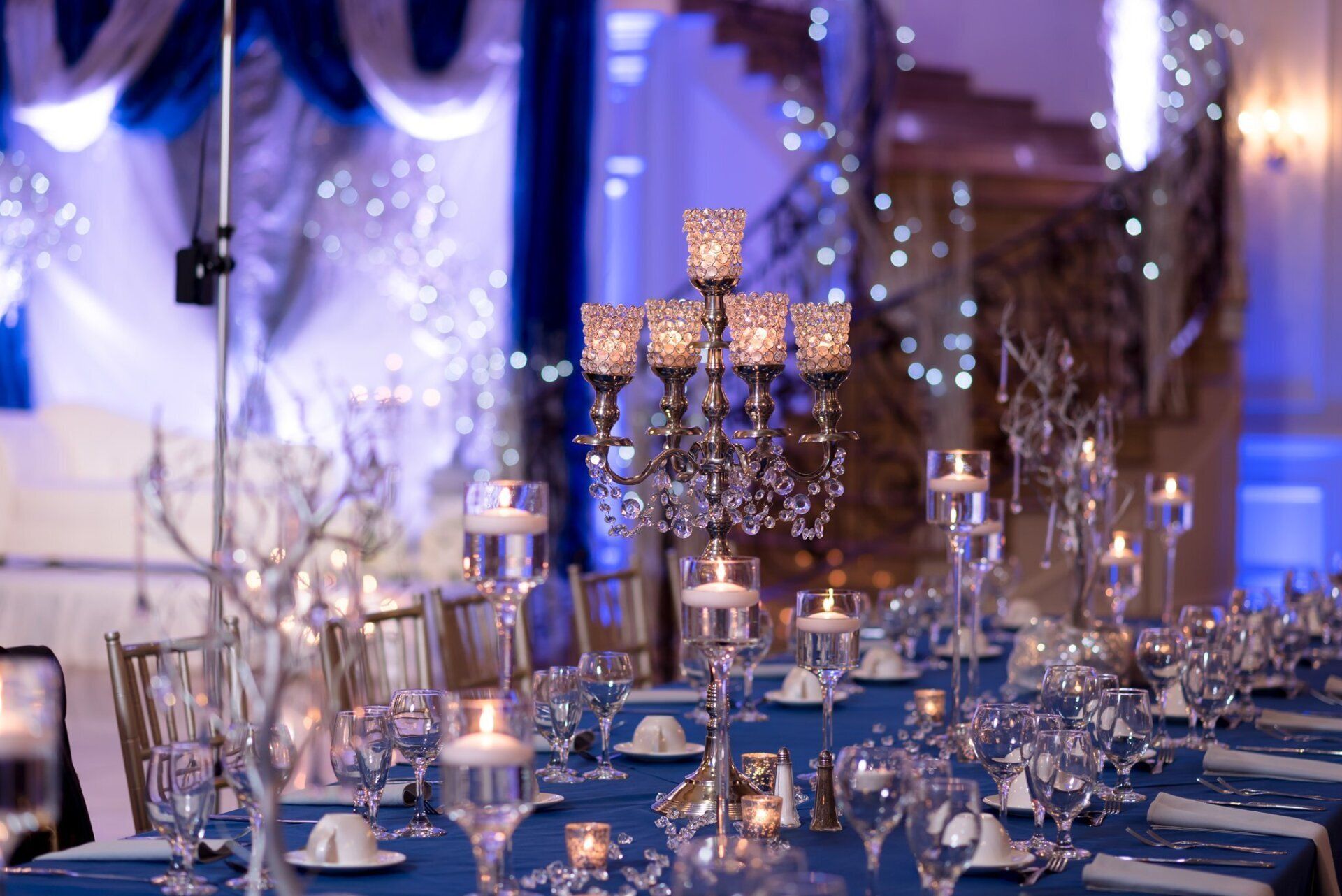 Blue-lit banquet table set with crystal glassware and gold candelabra centerpieces