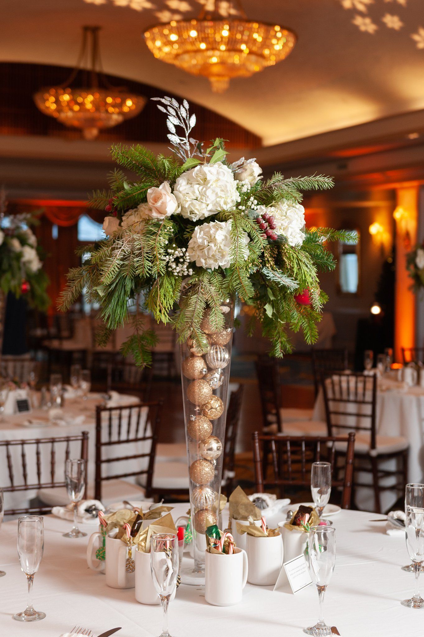 Tall white floral centerpiece on a decorated banquet table in a warmly lit event hall