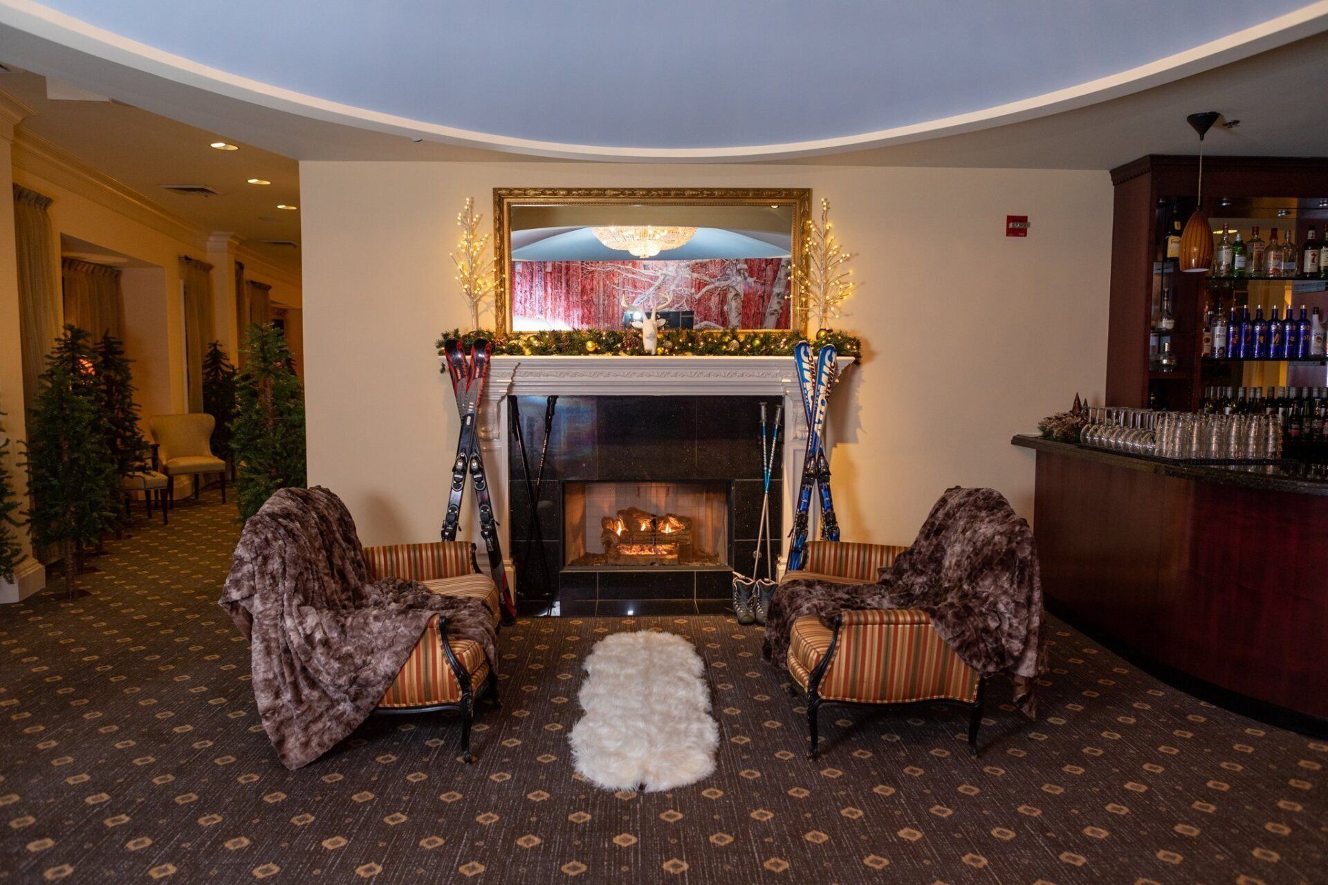 Lobby lounge with fireplace, two patterned chairs, and a bar in the background