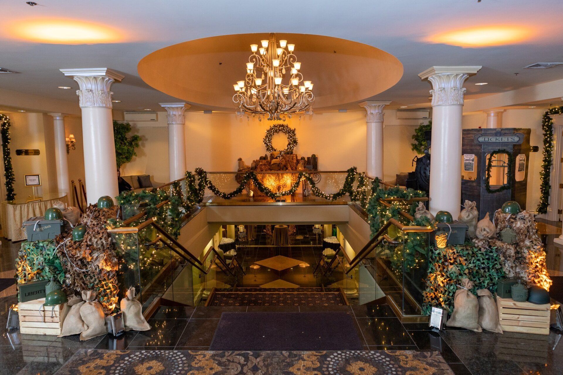 Elegant hotel lobby with chandelier, white columns, and grand staircase decorated with plants and flowers