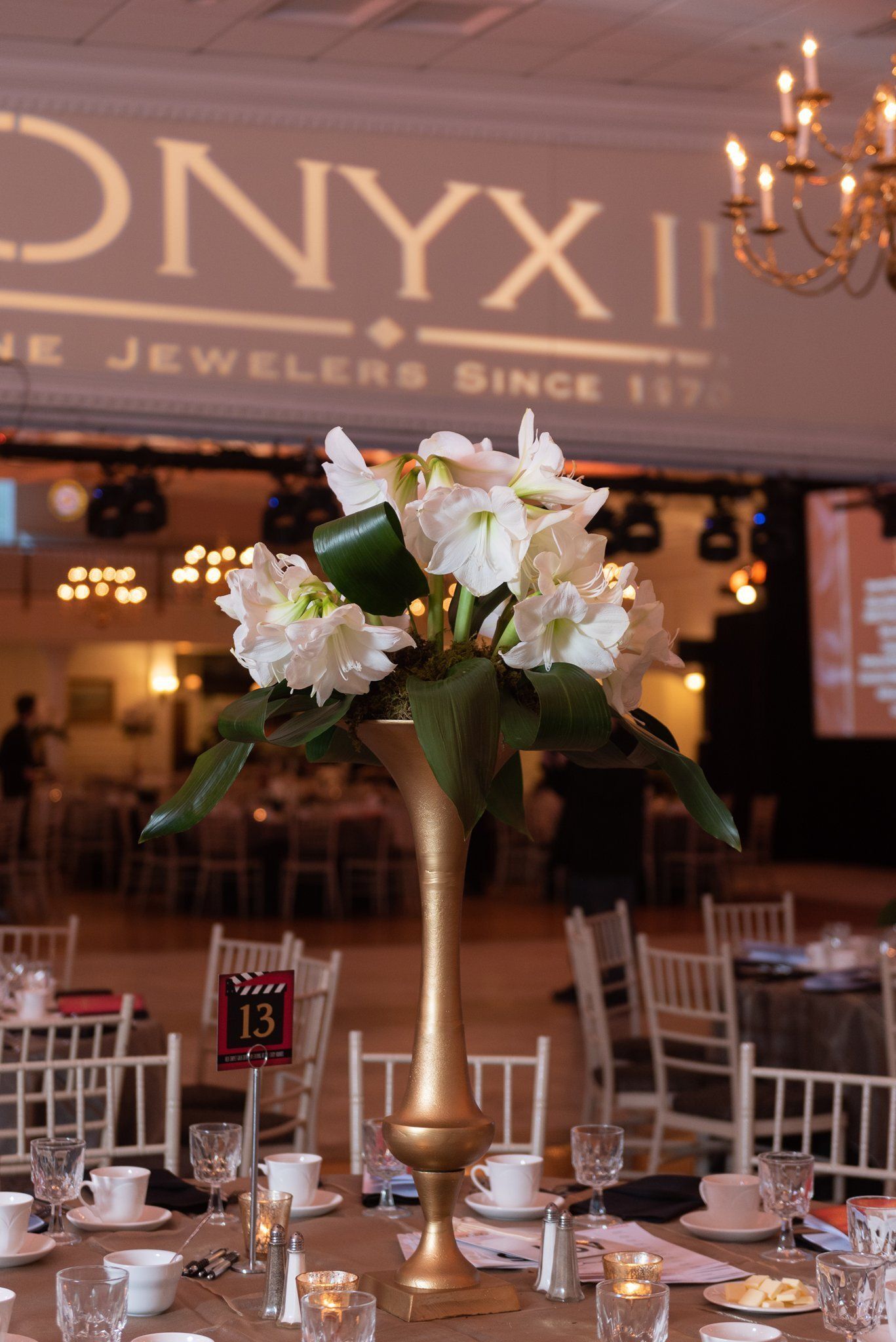 Banquet table with white floral centerpiece, candles, and gold decor in a jewelry store setting