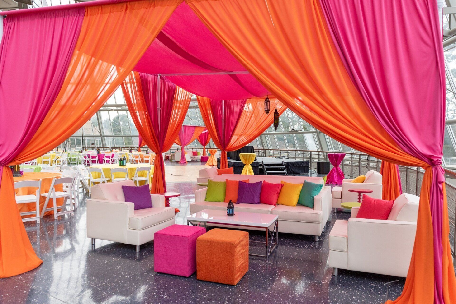 Colorful lounge with orange and pink drapes, white sofas, and bright seating in a decorated outdoor venue