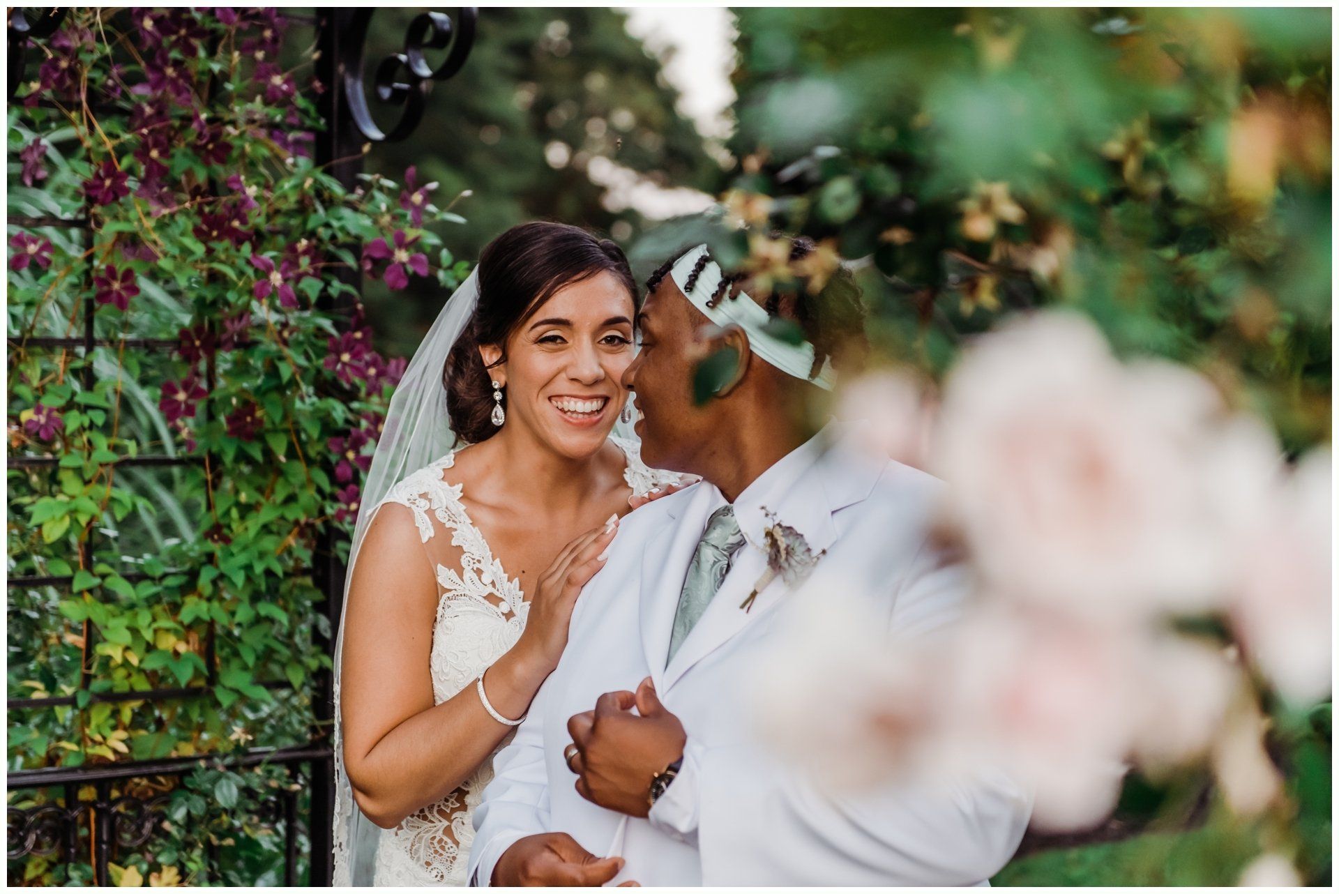 Bride and groom smiling in a garden, with the groom kissing the bride's cheek.
