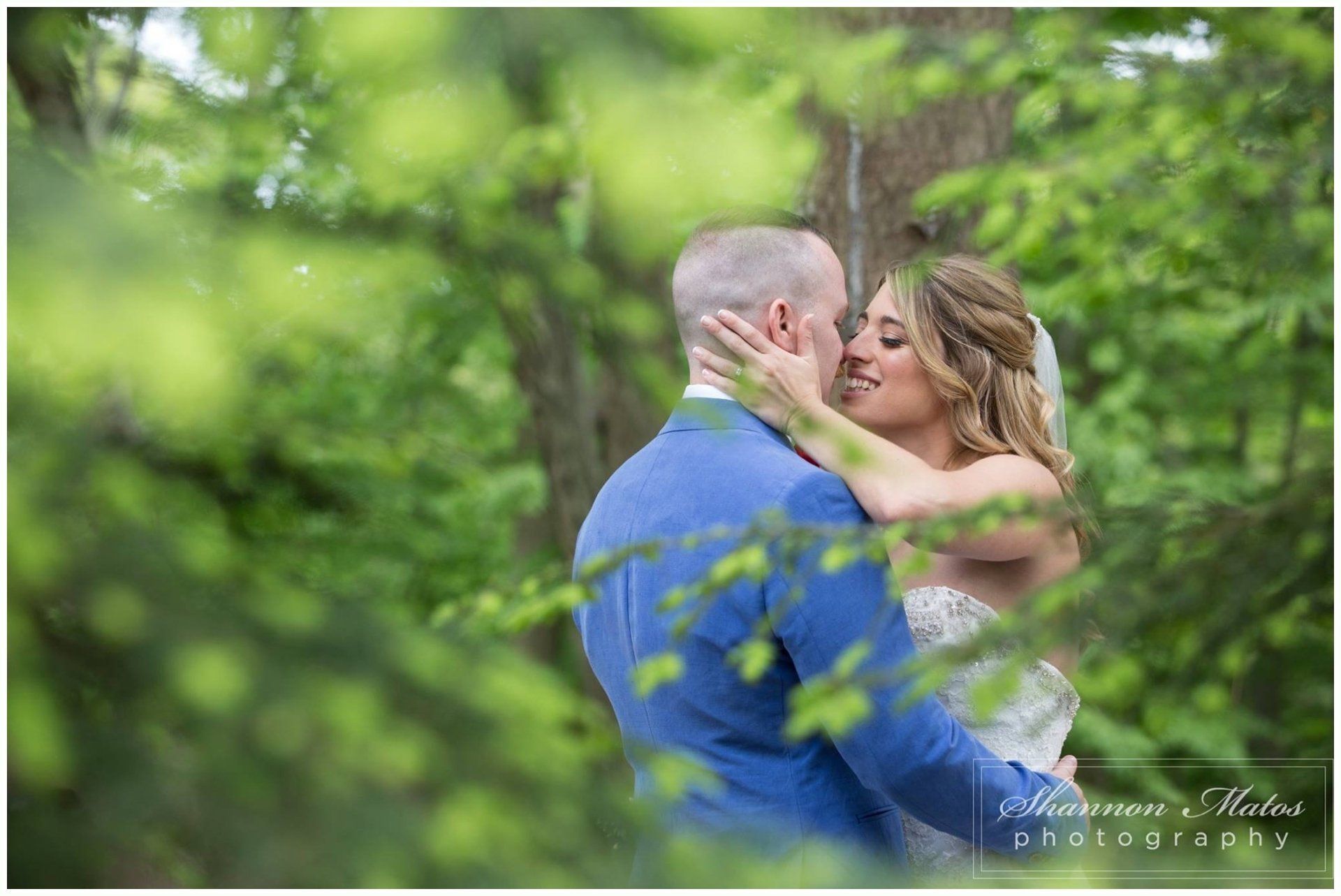 Couple embracing in a lush green outdoor setting, with the woman touching the man’s face.