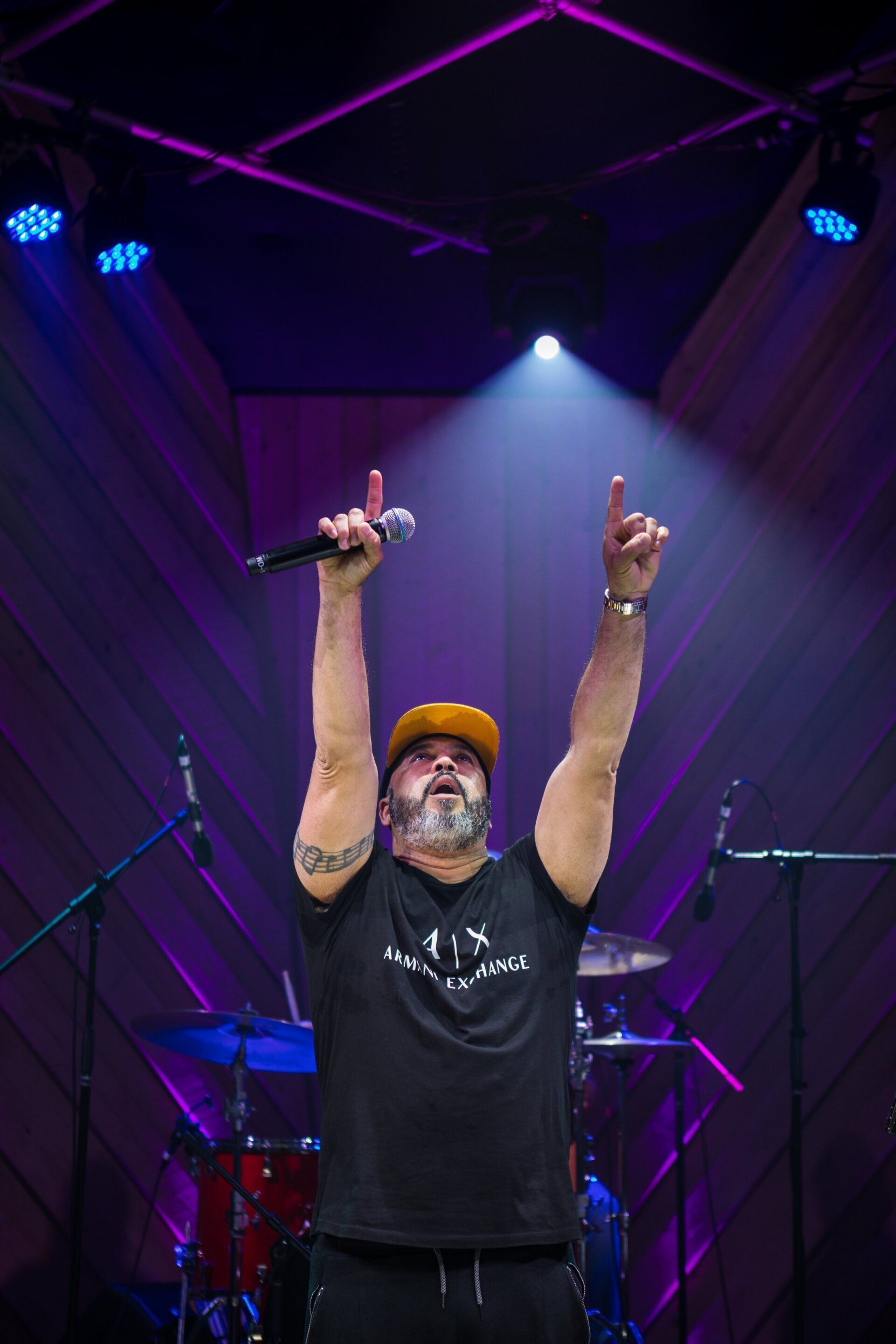 Singer on stage under purple lights, raising both arms and holding a microphone.
