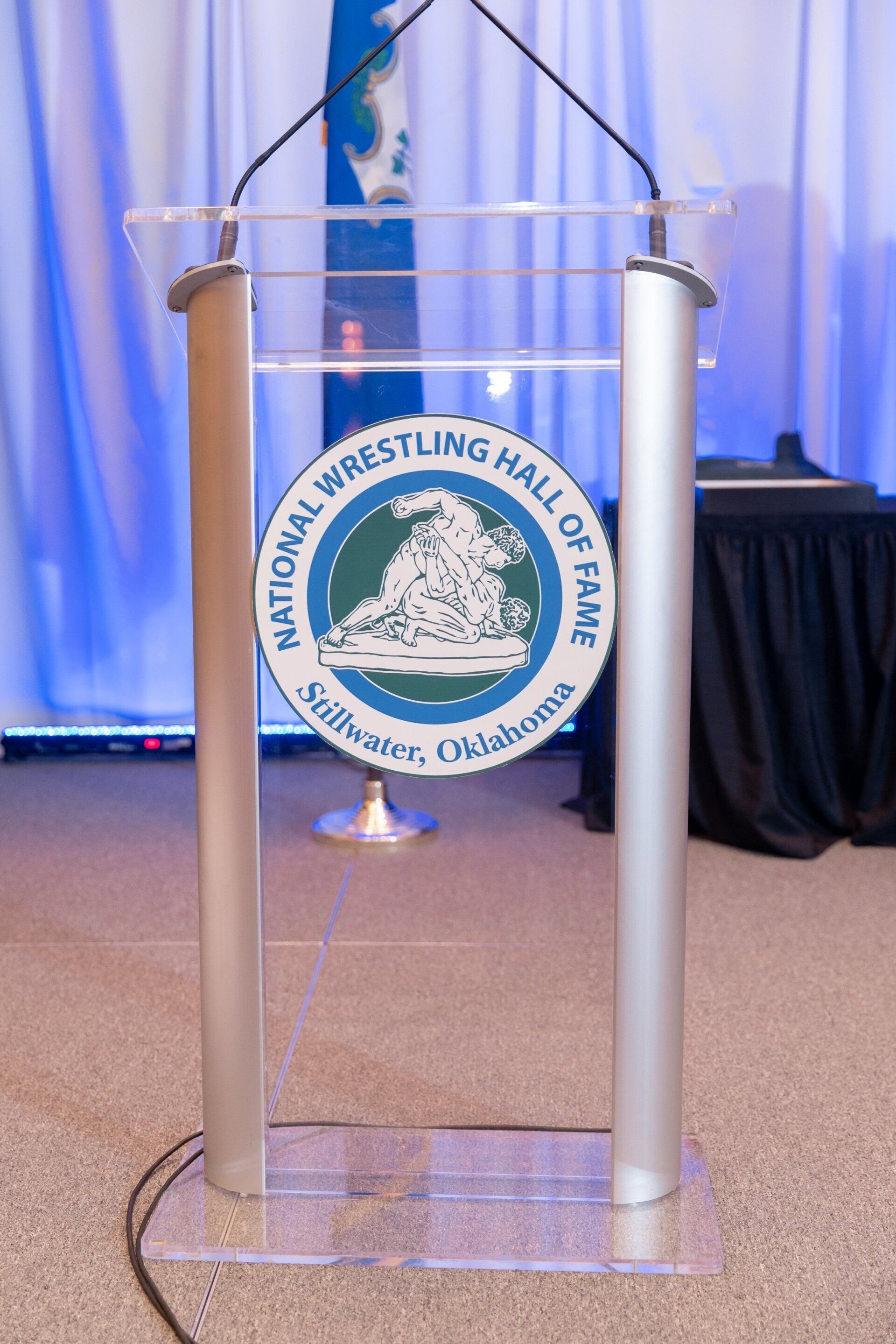 Clear podium with National Wrestling Hall of Fame emblem on a stage with blue curtains