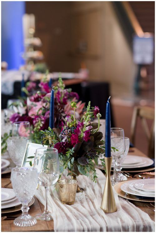 Elegant dining table with floral centerpiece, glassware, gold candlesticks, and blue taper candles