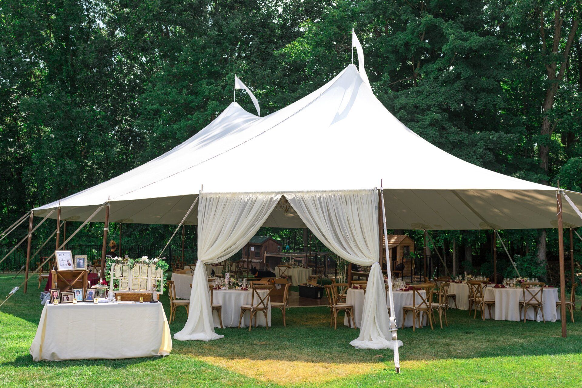 White event tent with draped entrance and tables set up on a green lawn under trees