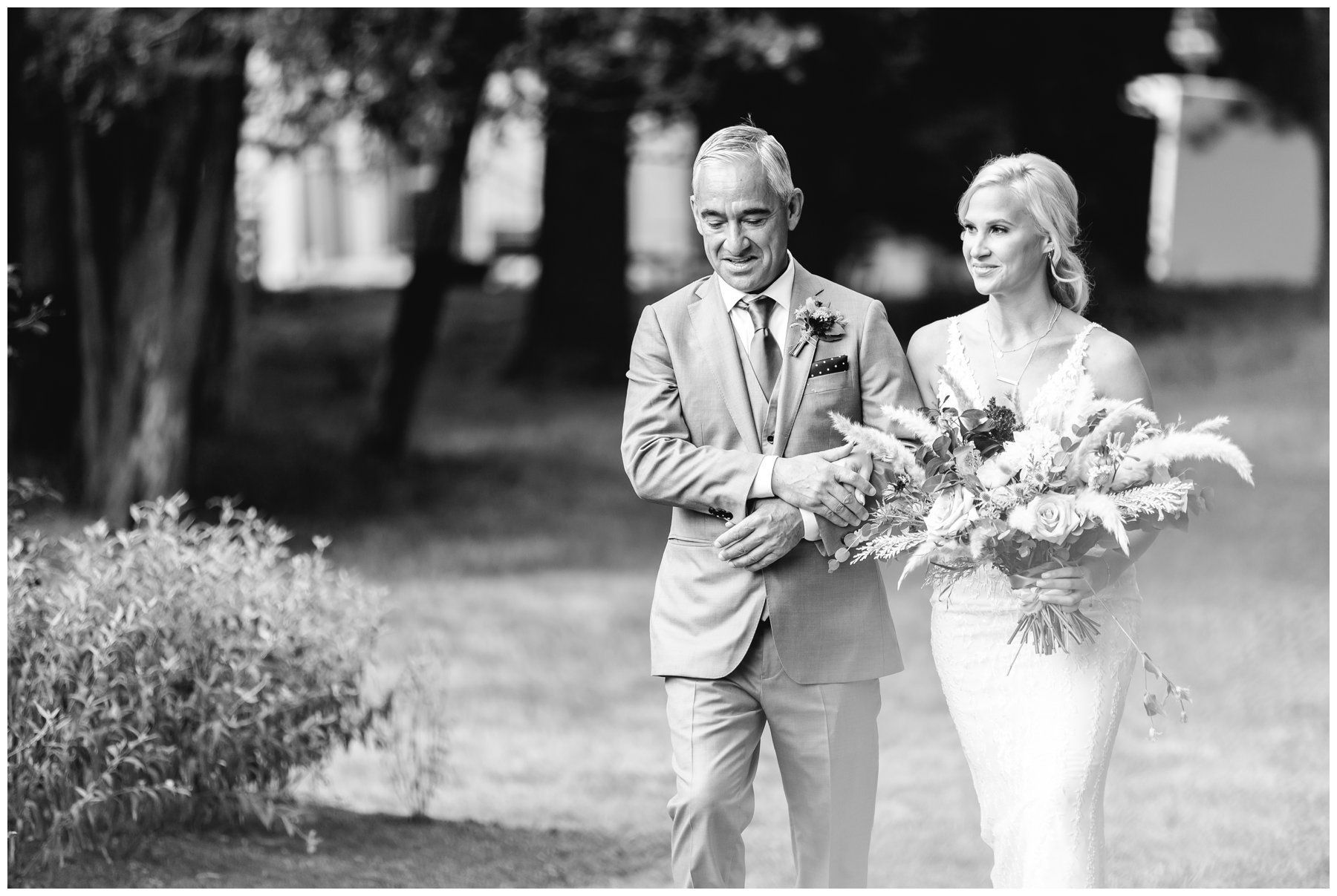 Bride and groom walking outdoors holding bouquets, smiling in a garden setting