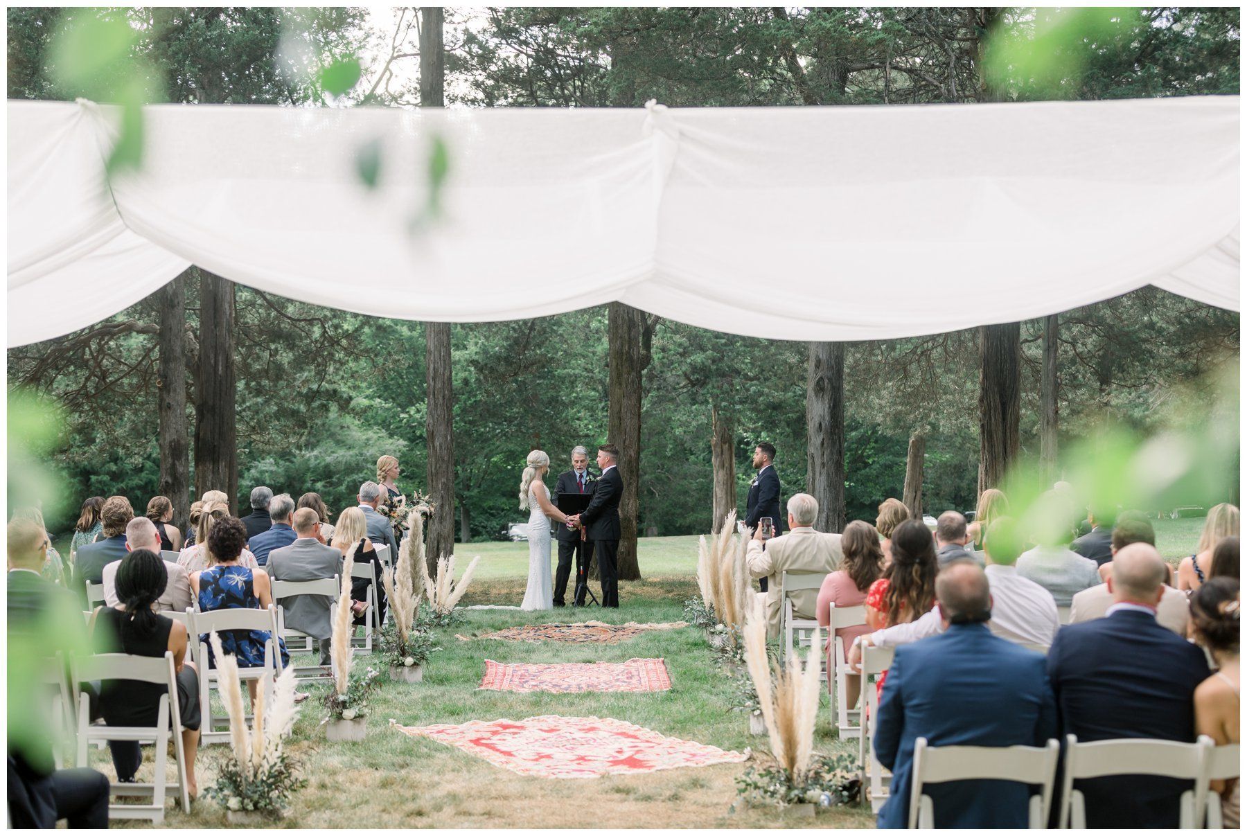 Outdoor wedding ceremony under white drapes with seated guests and a couple at the altar
