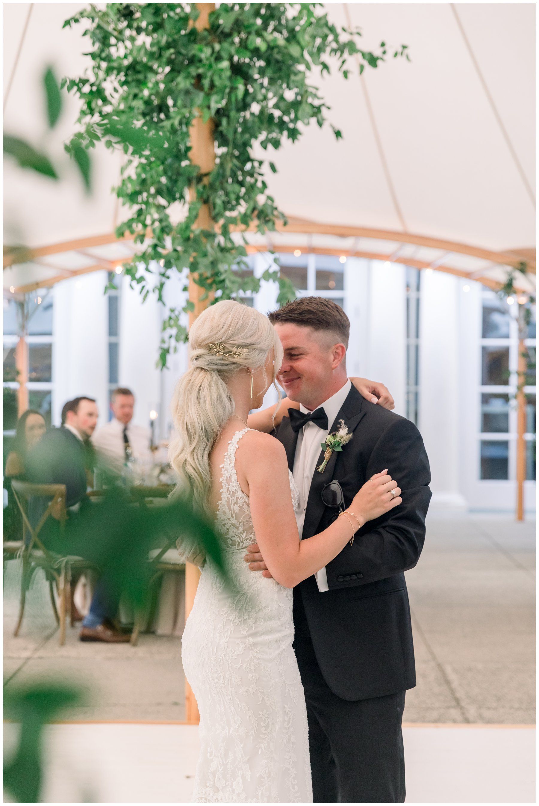 Bride and groom slow dancing beneath a tent at an outdoor wedding reception