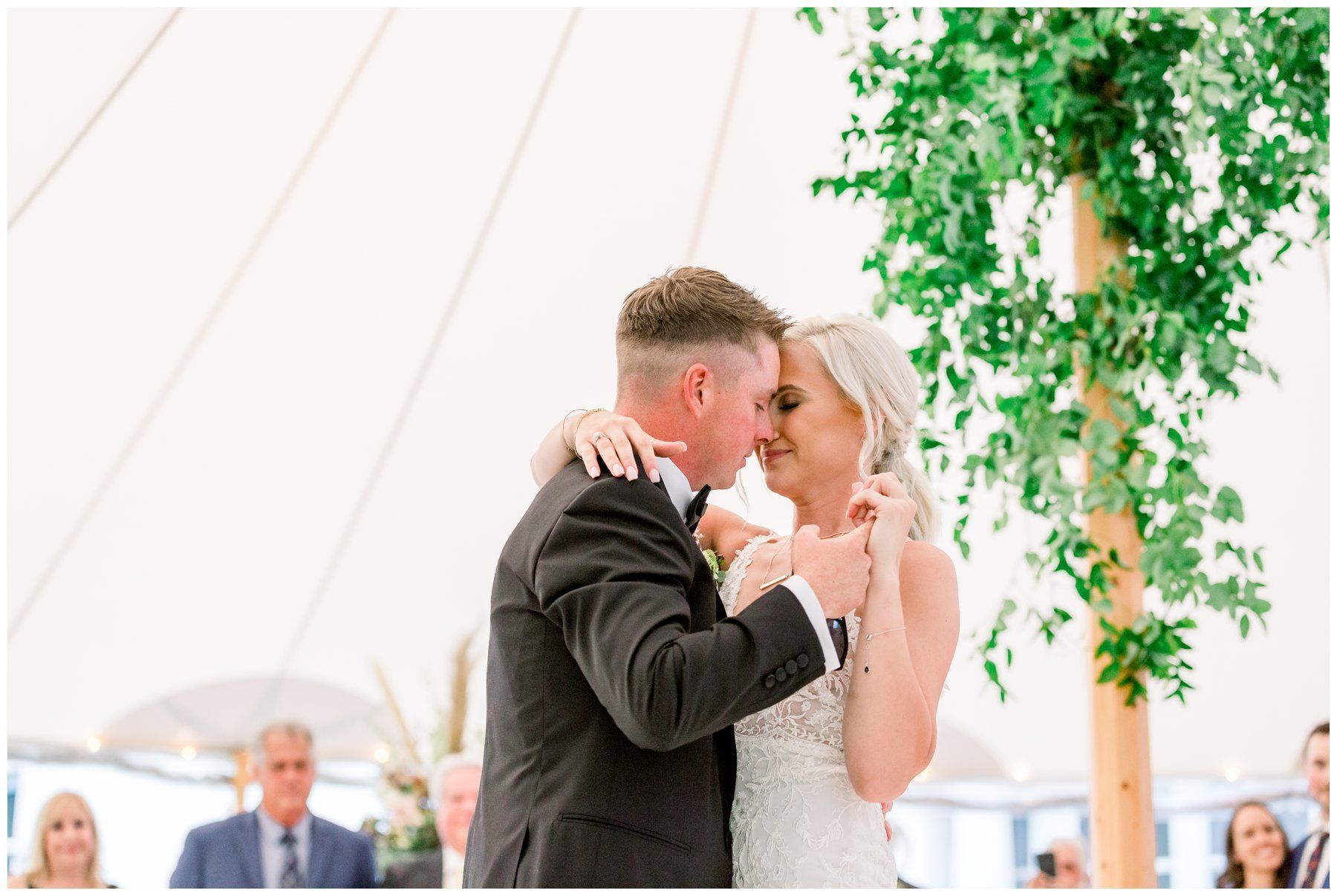 Bride and groom share a kiss at a wedding ceremony under a white tent with greenery