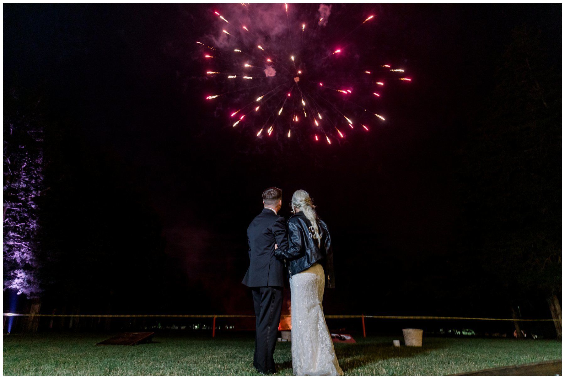 Couple standing together outdoors under pink fireworks at night