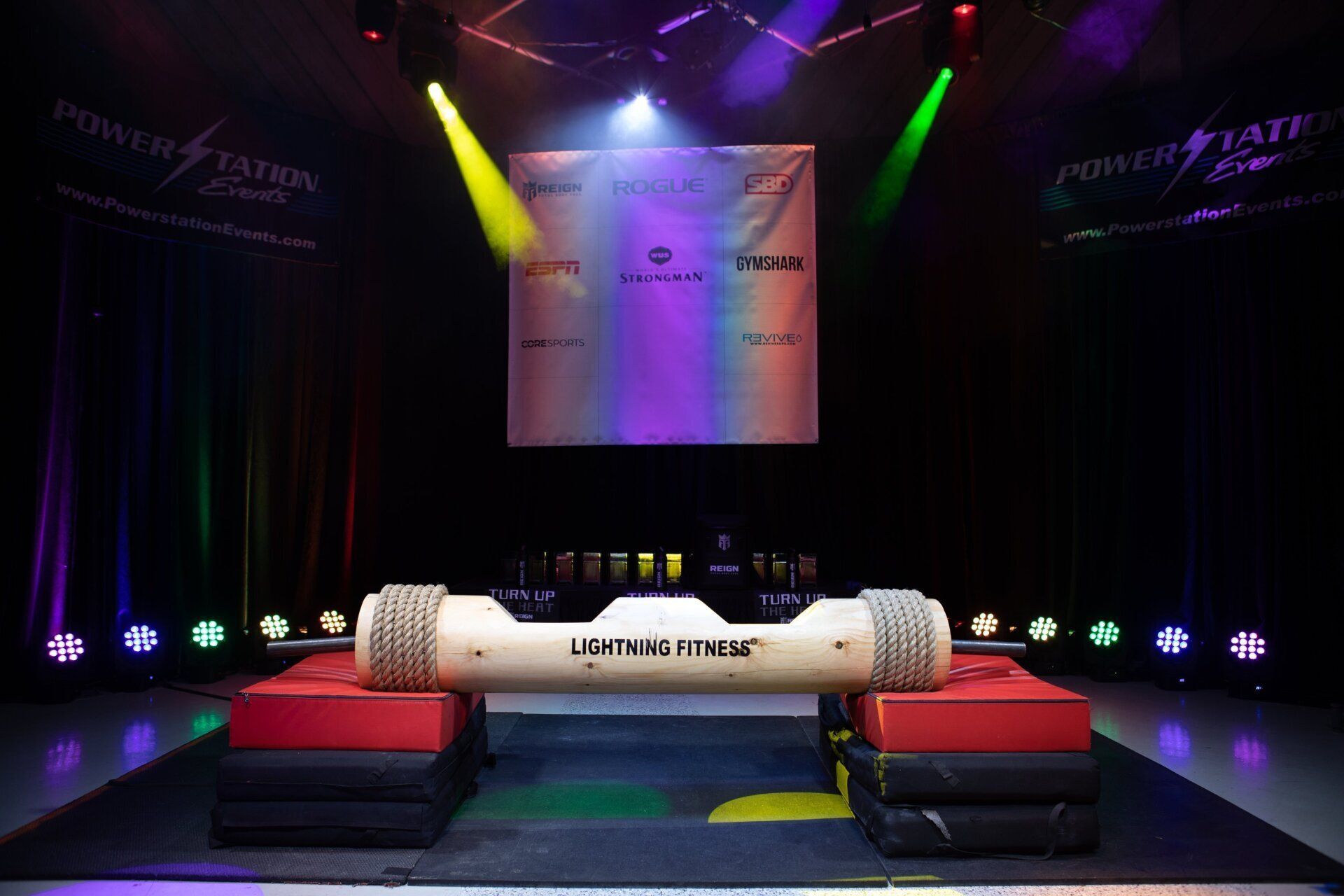 Empty stage with colorful spotlights, black curtains, red benches, and a white cylindrical prop in the center