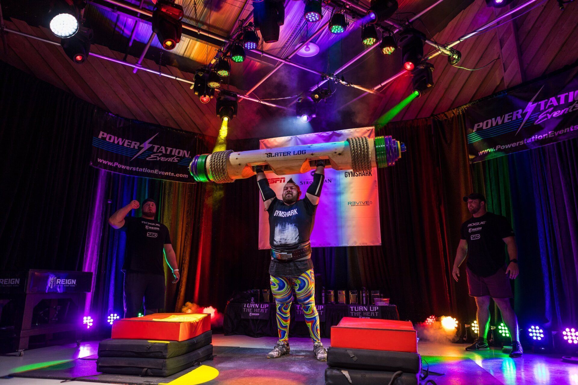 Person holding a giant prop bottle on a neon-lit stage with purple and red lights