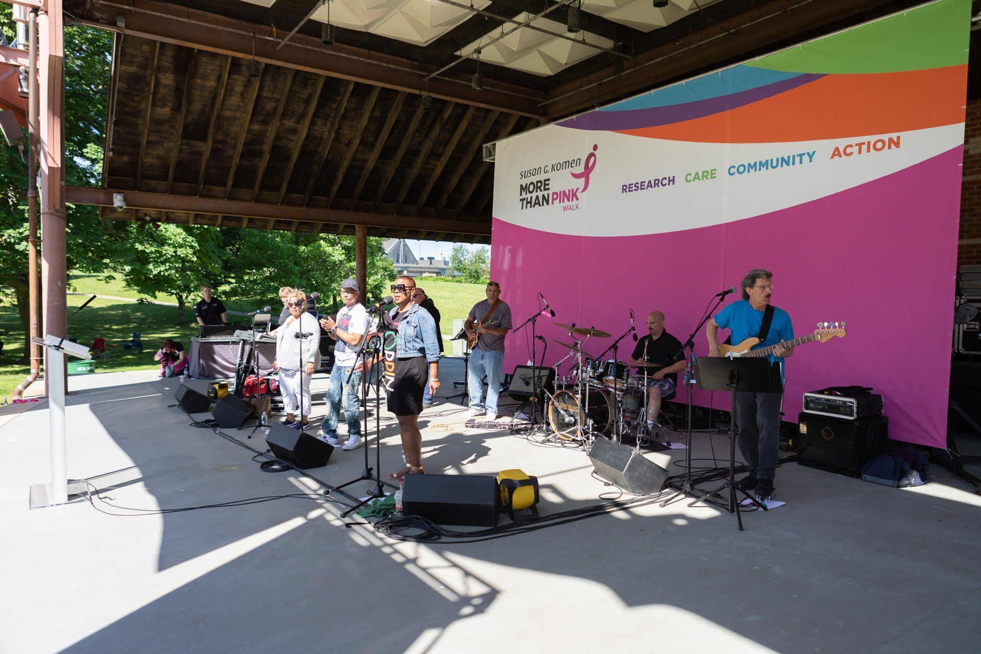 Live band performing on an outdoor stage with a bright pink backdrop and pavilion roof