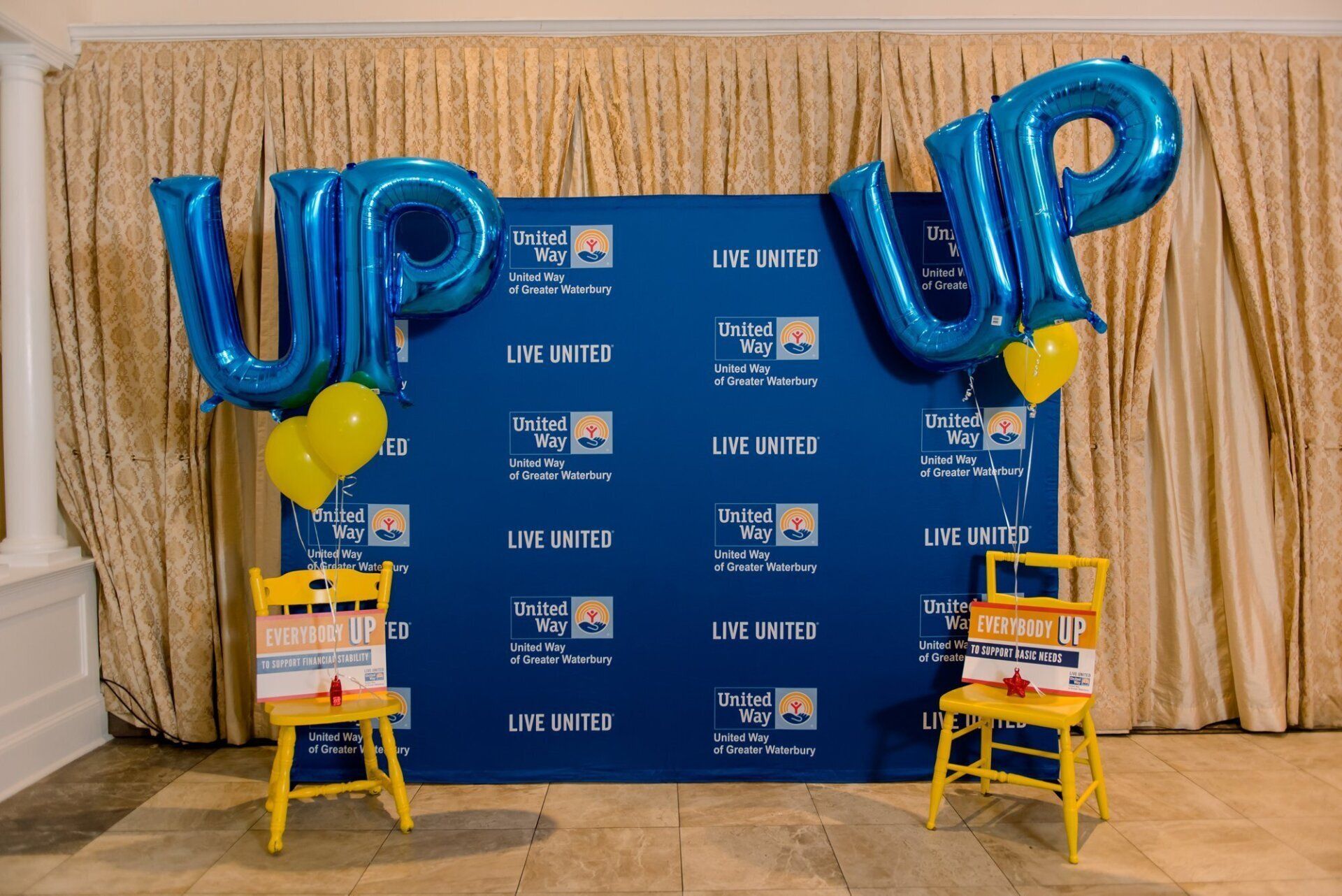 Blue “UP” balloon display with yellow balloons and small chairs in front of a branded backdrop