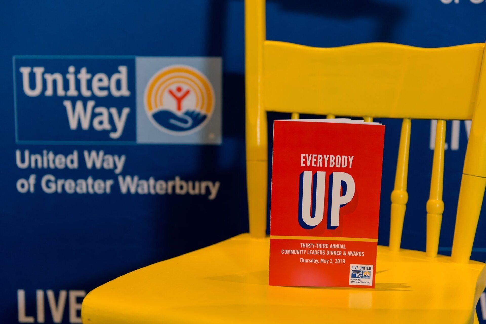 Yellow chair with a red “Everybody UP” booklet beside a United Way of Greater Waterbury sign