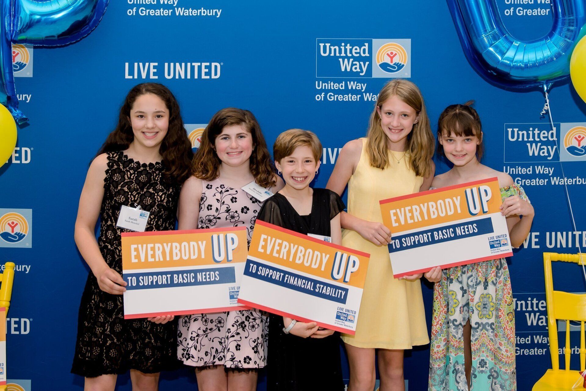Four girls holding “Everybody Up” signs at a United Way event backdrop