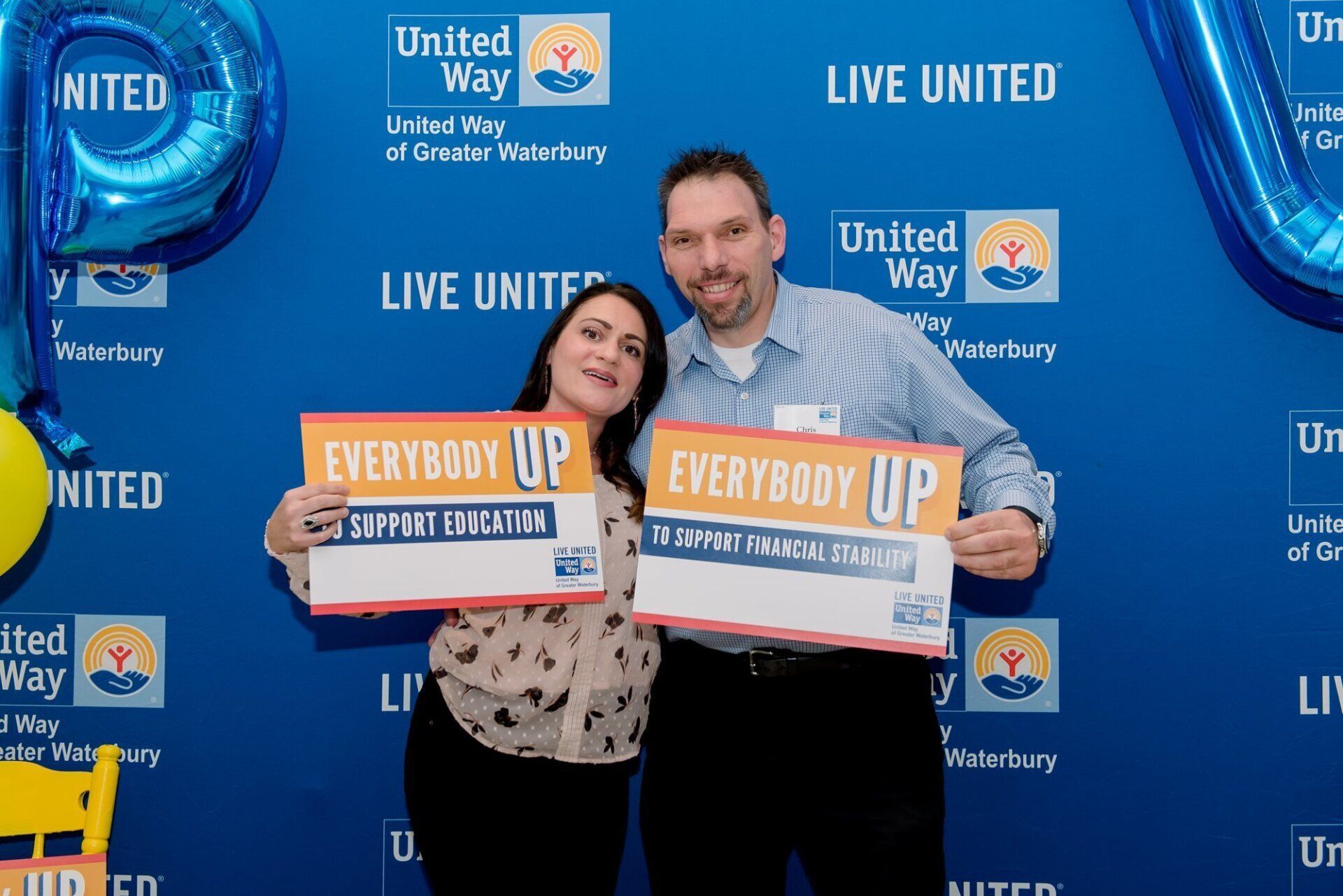 Two people holding “Everybody Up” signs in front of a United Way “Live United” backdrop.