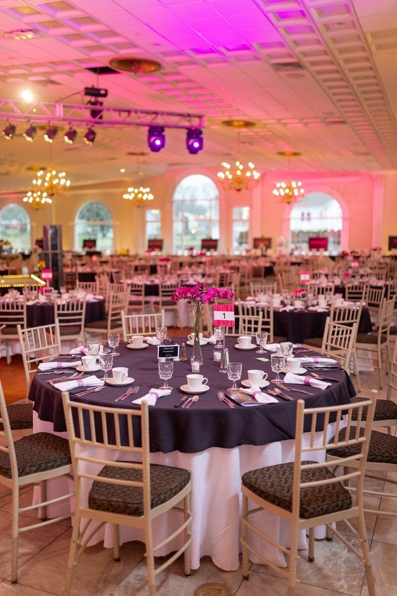Elegant banquet hall with round tables set for an event under pink and purple lighting