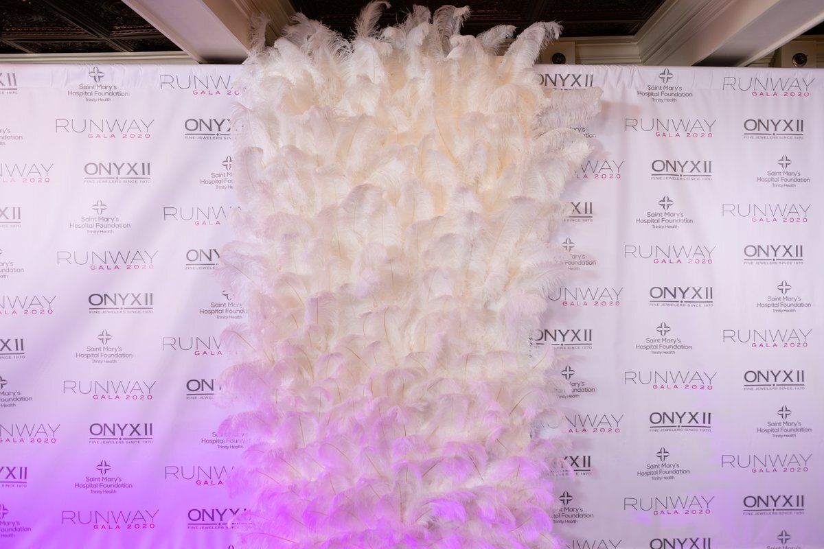 White feathered backdrop at a step-and-repeat event, lit with pink-purple lights
