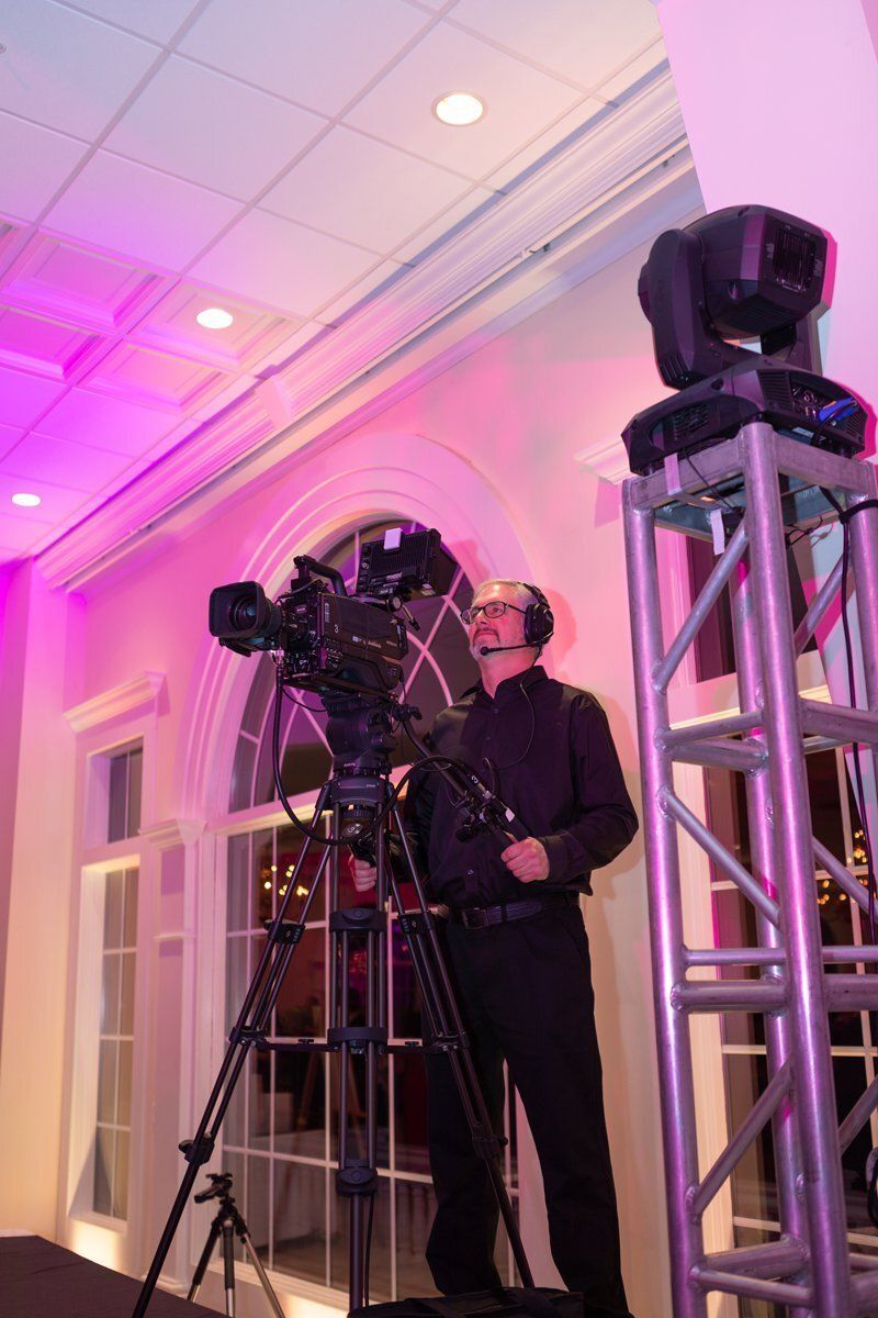 Person operating a large camera rig in a pink-lit room beside stage lighting truss
