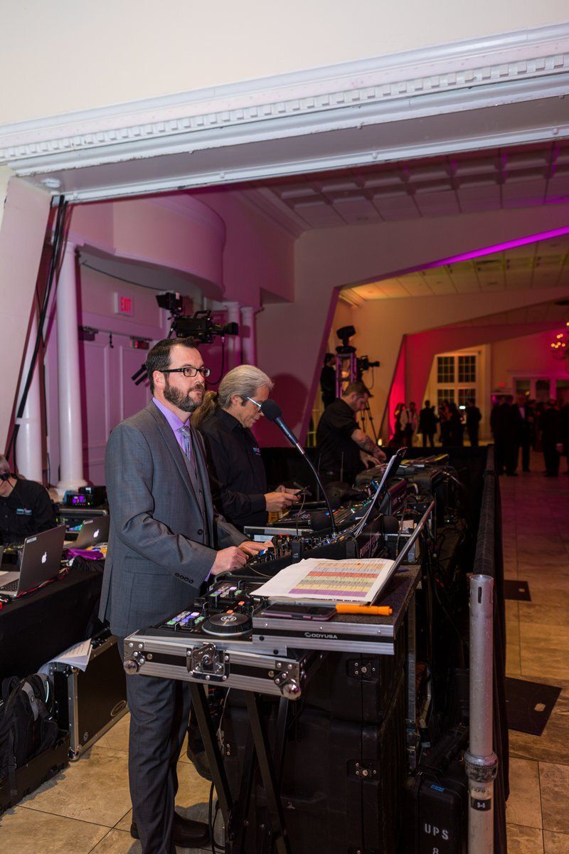 Musicians performing on a stage in a formal hall, with a keyboard player in the foreground under pink lighting