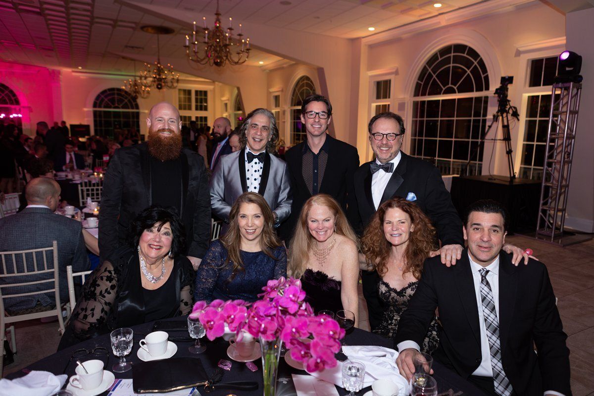 Formal group portrait at a banquet table with pink flowers in a warmly lit ballroom.