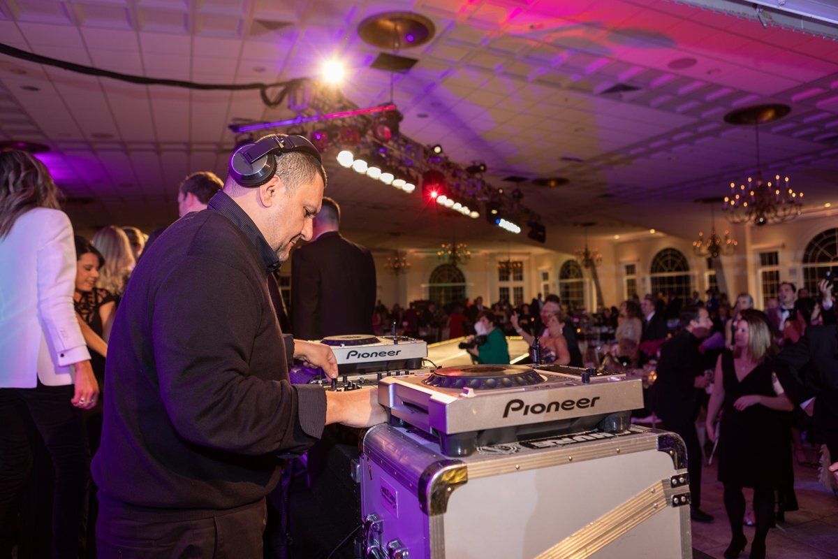 DJ performing at a lively indoor event with purple lighting and a crowd in the background