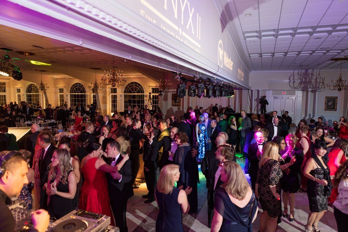 Crowded dance floor at a formal party, with guests dancing under purple and pink lighting.