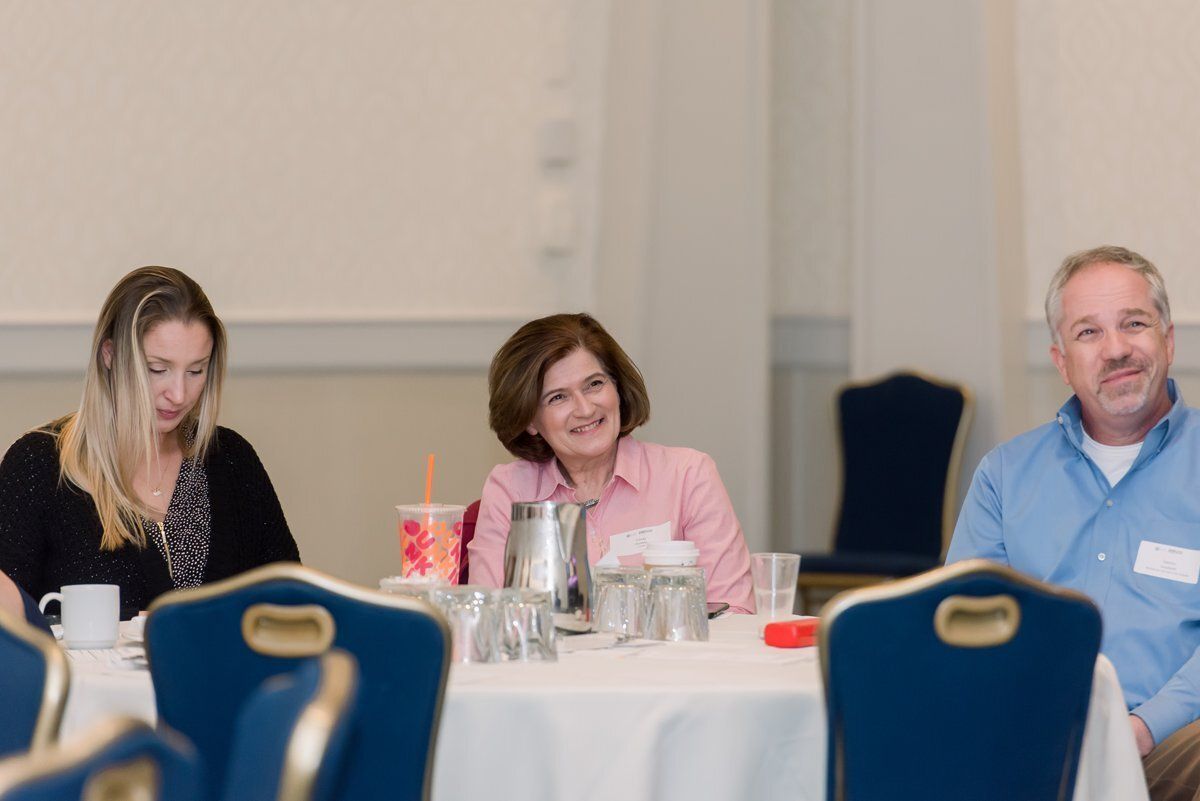 Three people seated at a table during a meeting, with glasses and water pitchers in front of them.