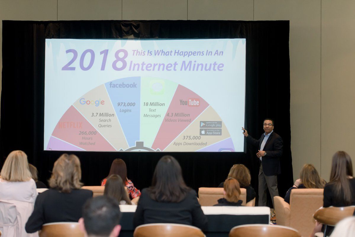 Presenter speaking beside a slide titled “2018 What’s Happening in Air Internet Minute” to an audience.