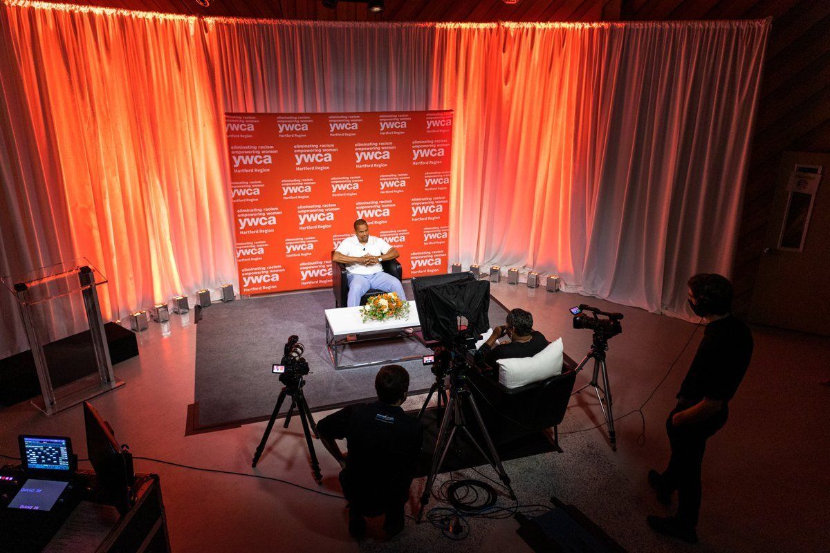Interview set with red backdrop, curtains, and cameras filming a seated speaker under studio lights