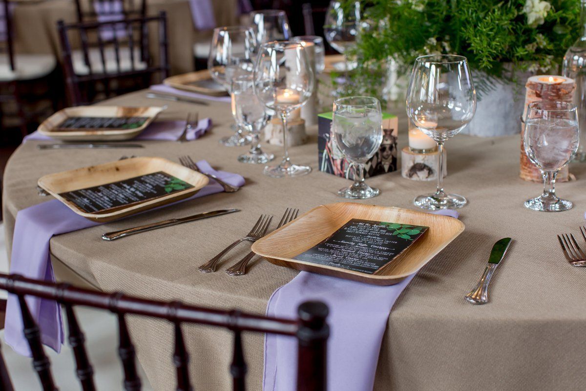 Set dining table with beige cloth, purple napkins, glassware, and floral centerpiece