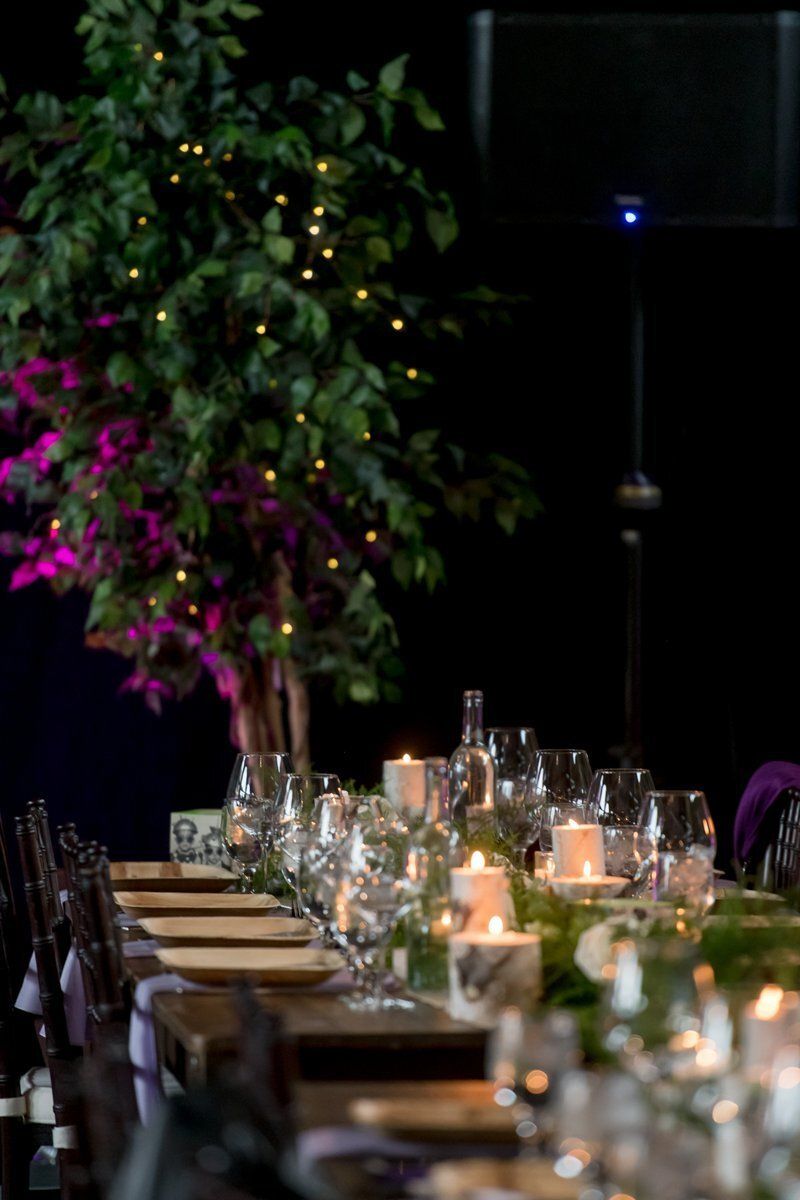 Elegant dinner table with candles, glassware, and a tall floral arrangement in a dimly lit room