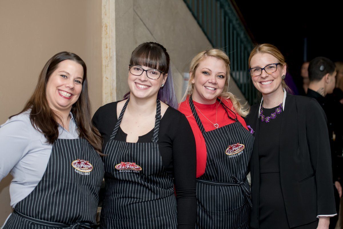 Four people in matching striped aprons smile at an indoor event.