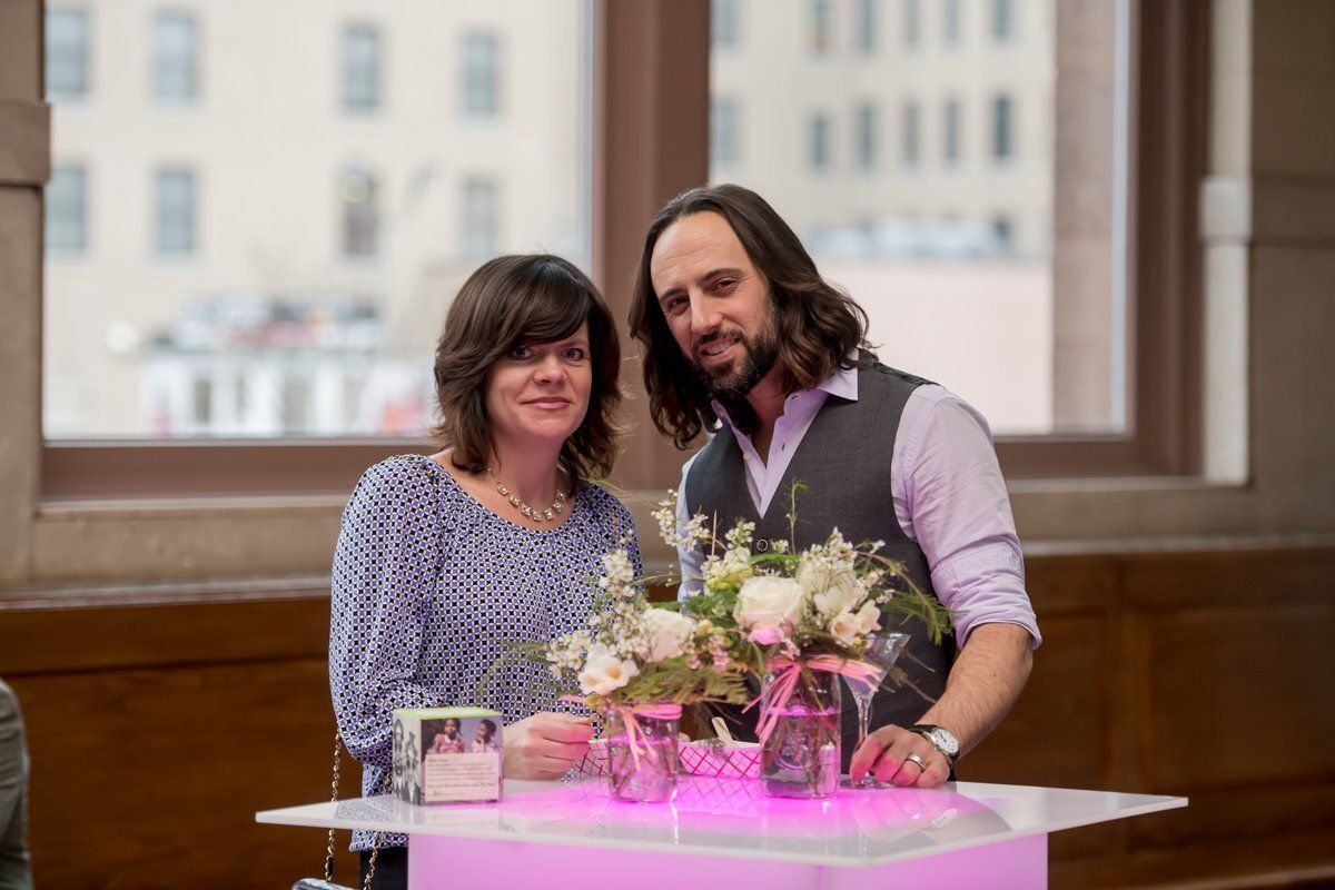 Two people standing behind a flower-decorated table indoors, smiling at the camera.