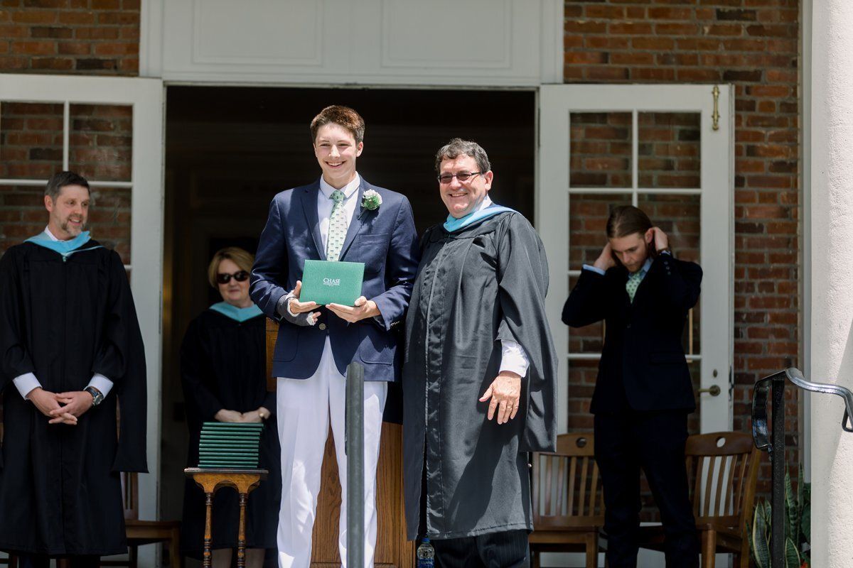 Graduation ceremony on a building stoop, with two people holding diplomas and others standing nearby.