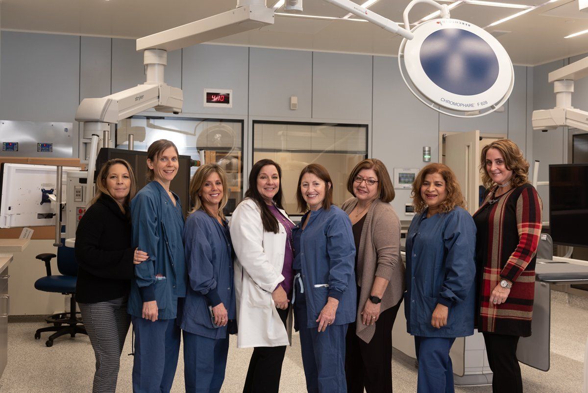 Group of seven healthcare workers standing in a dental clinic, smiling under bright examination lights.
