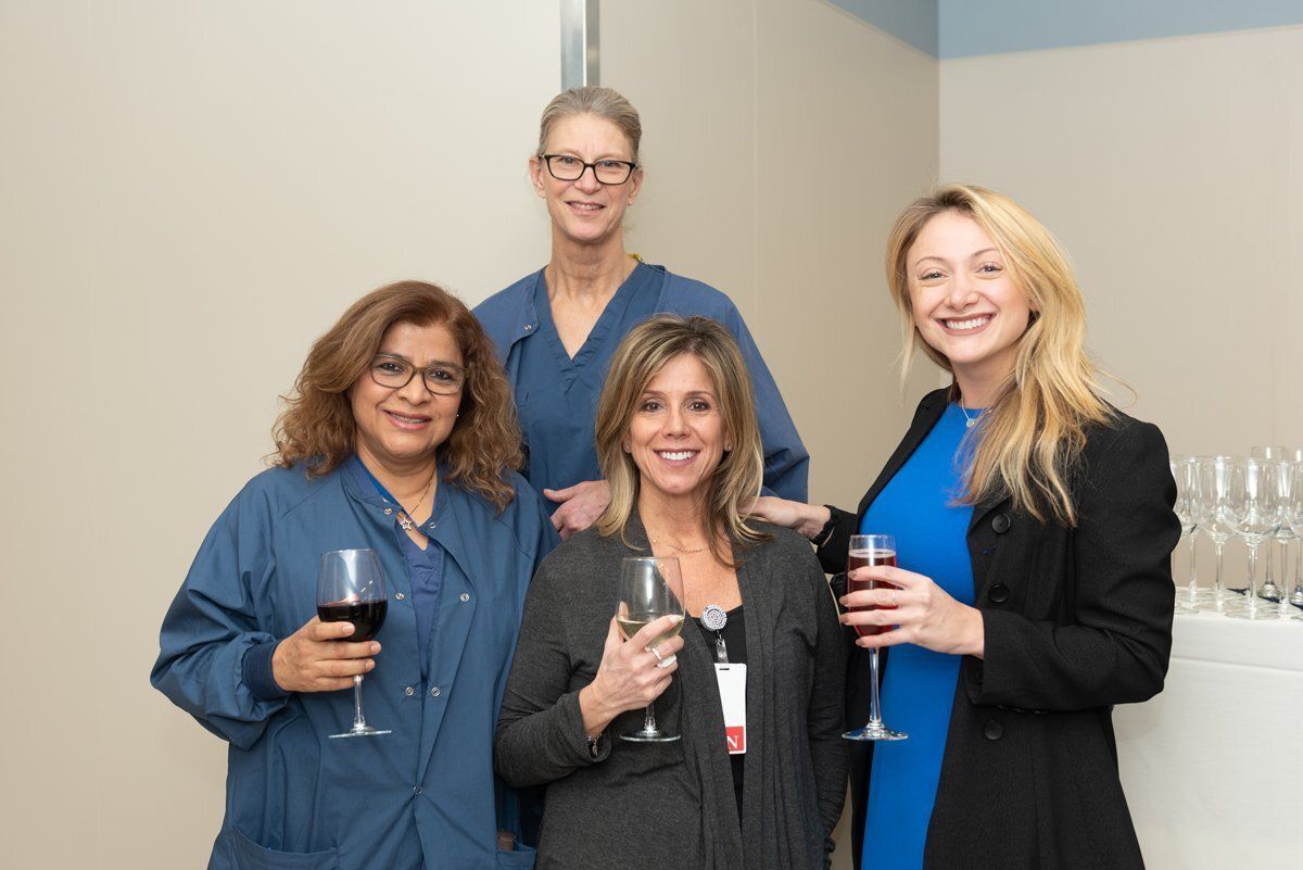 Four colleagues smiling and holding drinks in an office hallway