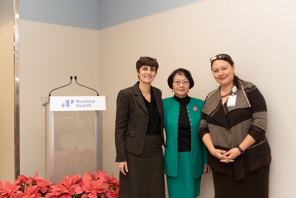 Three people standing beside a podium in a conference room, with red flowers in front.