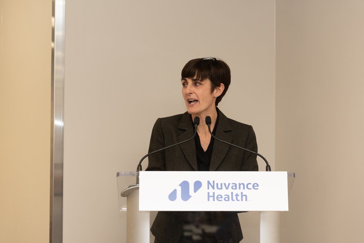 Speaker at a podium with a Nuance Health sign, speaking in a conference setting.