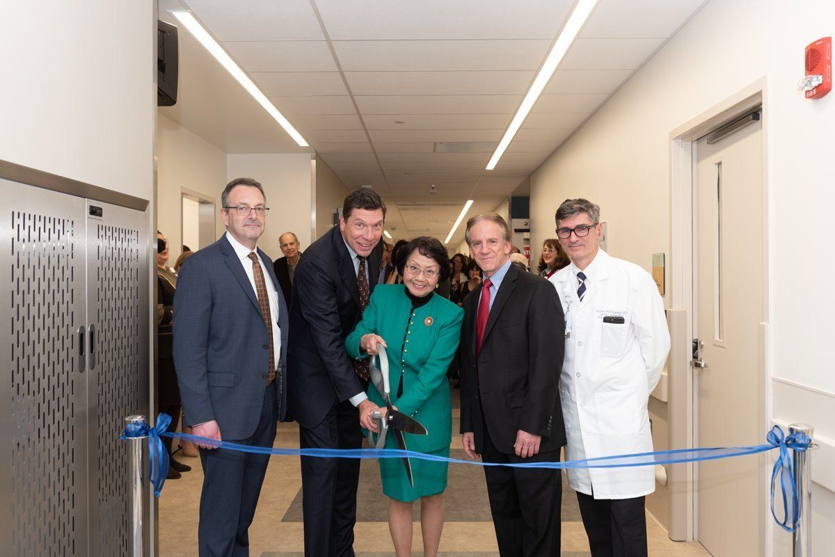 Ribbon-cutting ceremony in a hallway with five people standing behind a blue ribbon barrier.