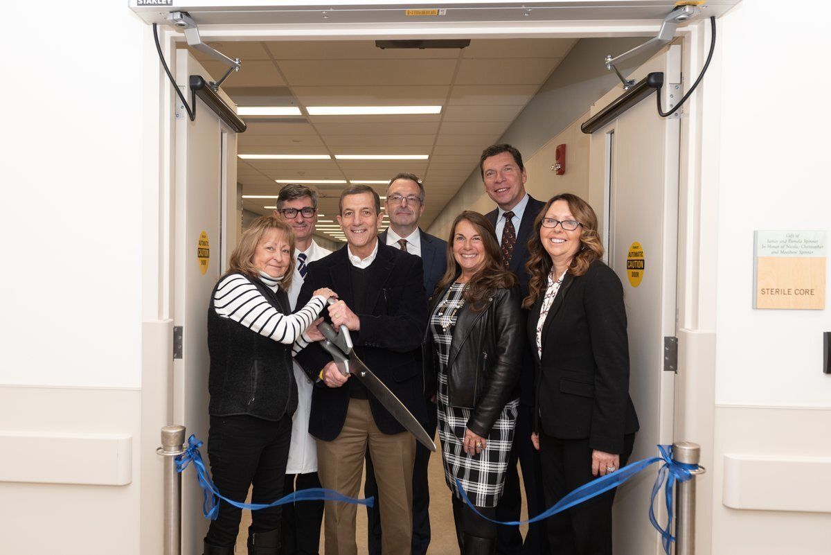 Group of five people posing in a doorway, holding scissors and smiling at a ribbon-cutting ceremony.