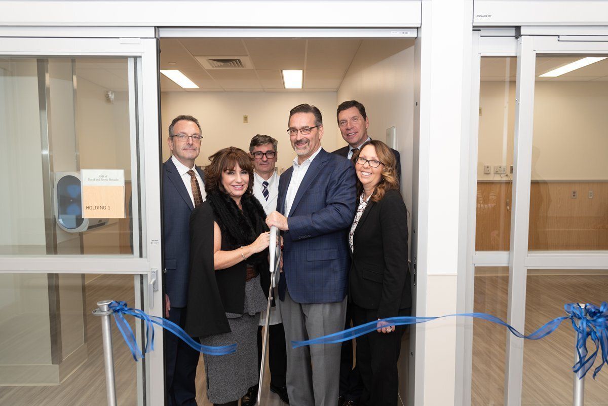 Group of people standing at a ribbon-cutting ceremony in a doorway, smiling and posing indoors.