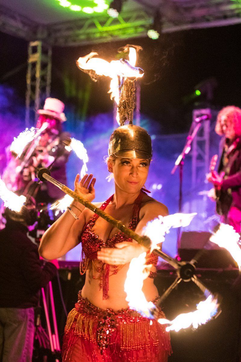 Fire dancer performing with flaming staffs on a brightly lit stage with purple and green lights