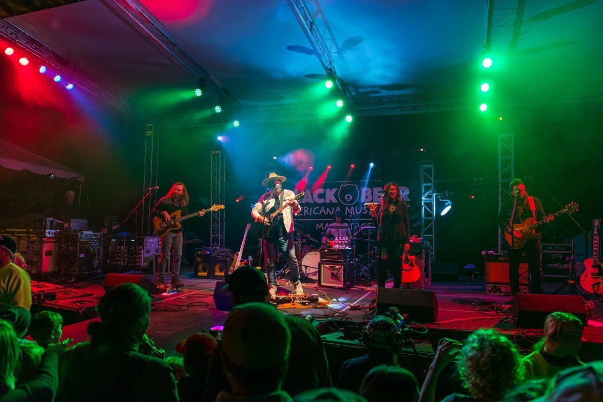 Live band performing on stage under red and green lights, with a crowd watching in front.