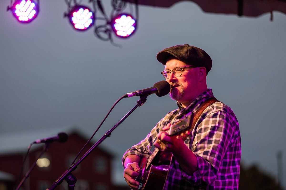 Musician singing and playing guitar on stage under purple lights
